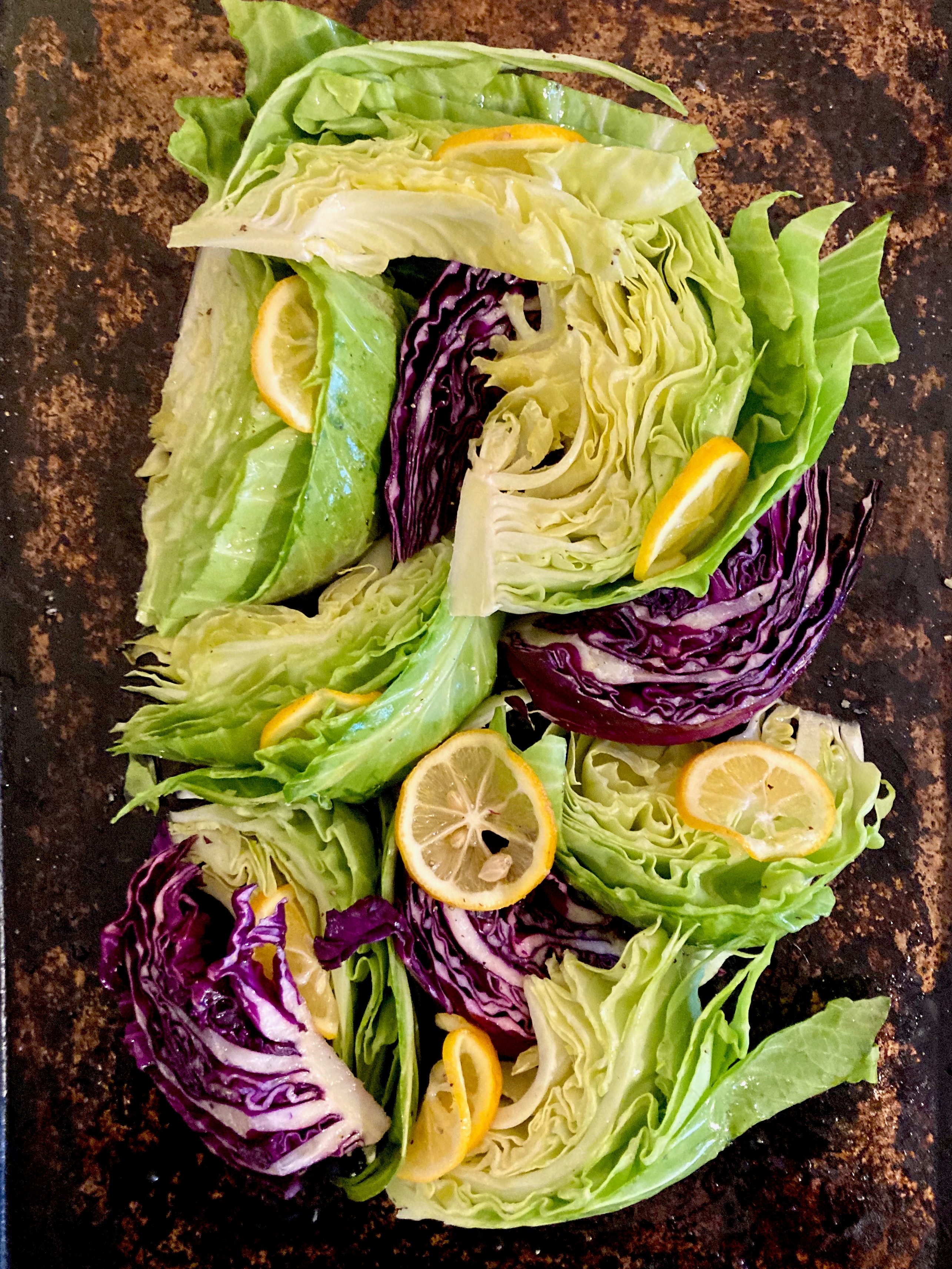 Roasted cabbage wedges and lettuce with lemon slices on a baking sheet