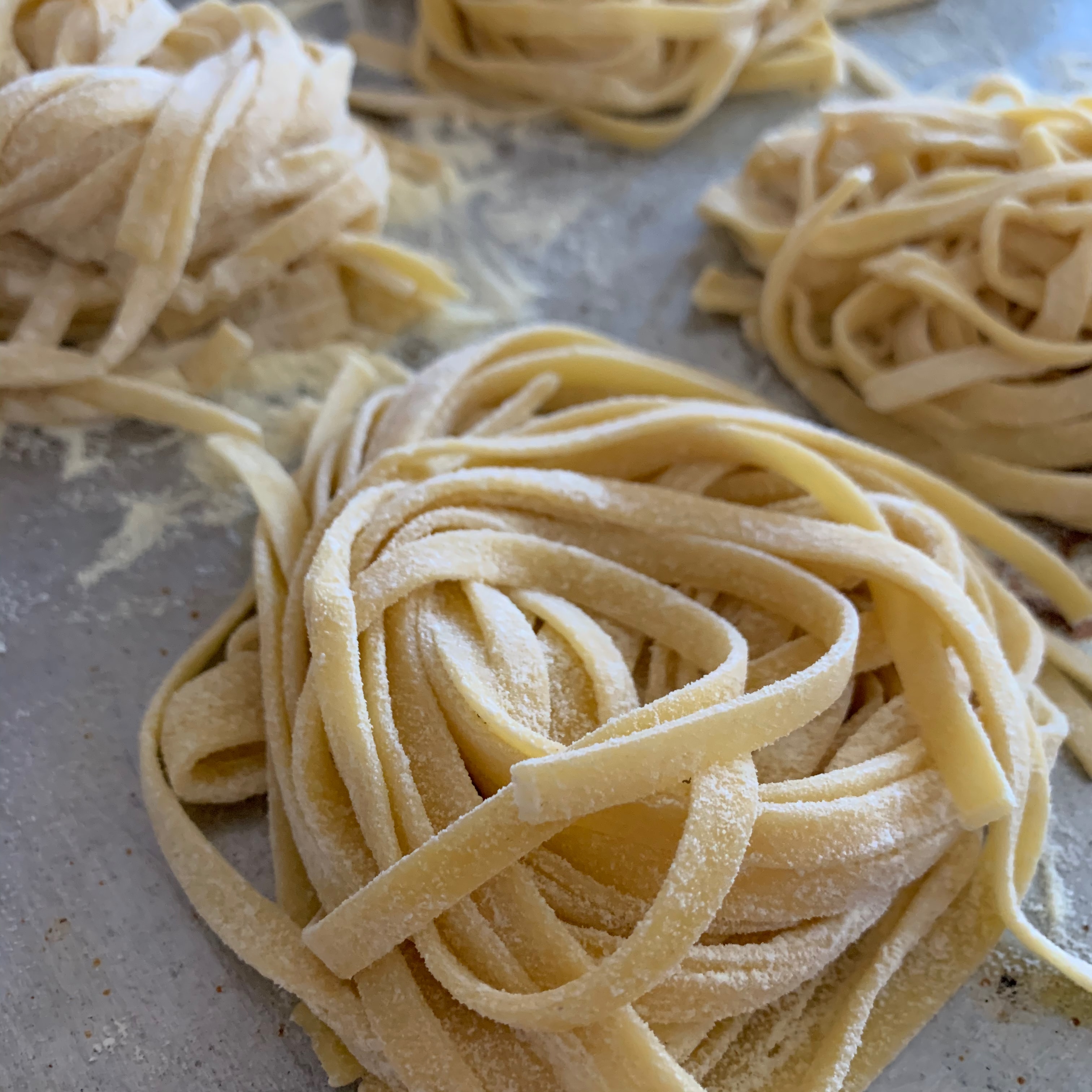 Fresh fettuccine nests dusted with flour on a work surface
